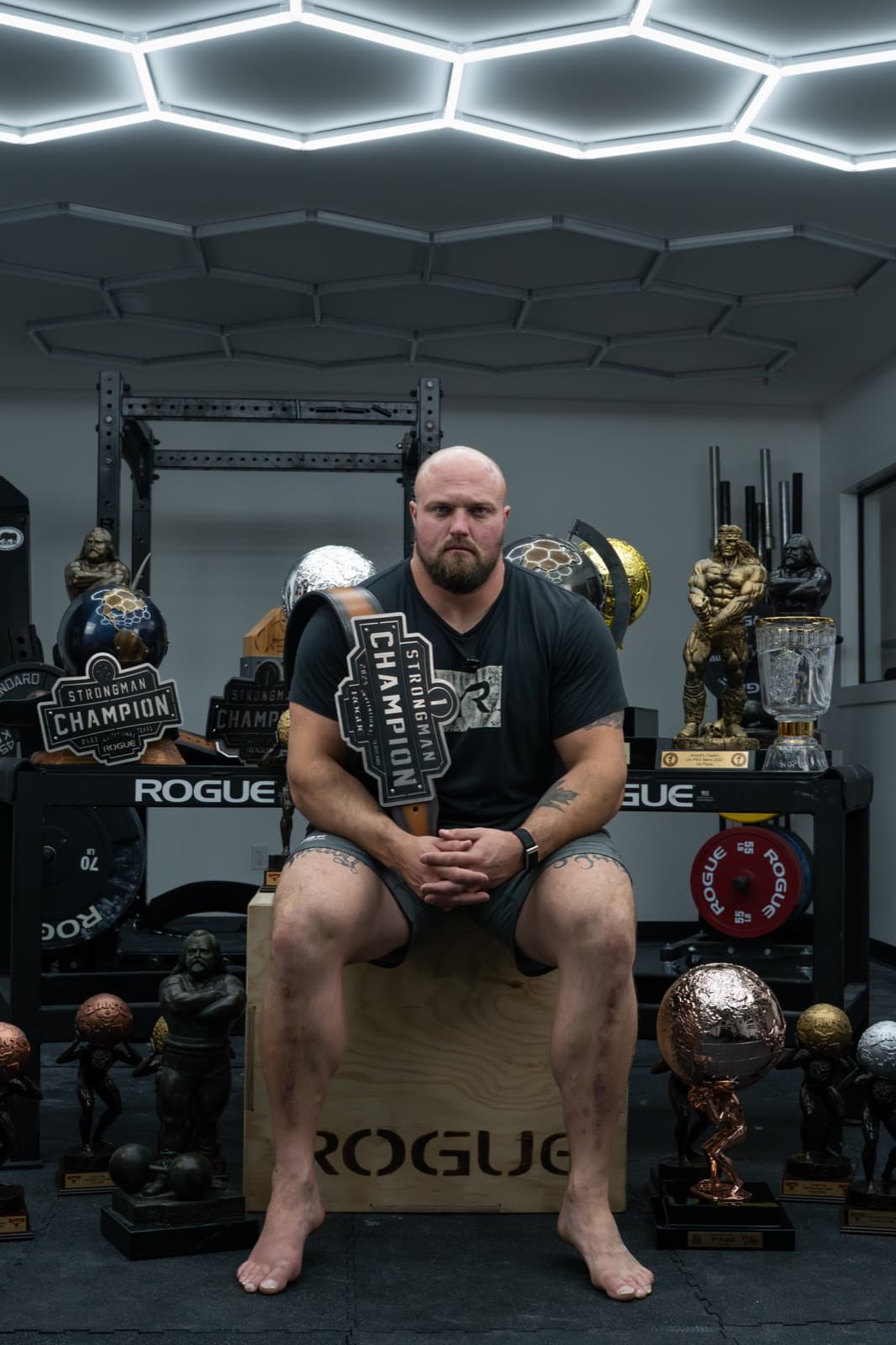 Mitchell Hooper seated in his gym surrounded by his strongman trophies