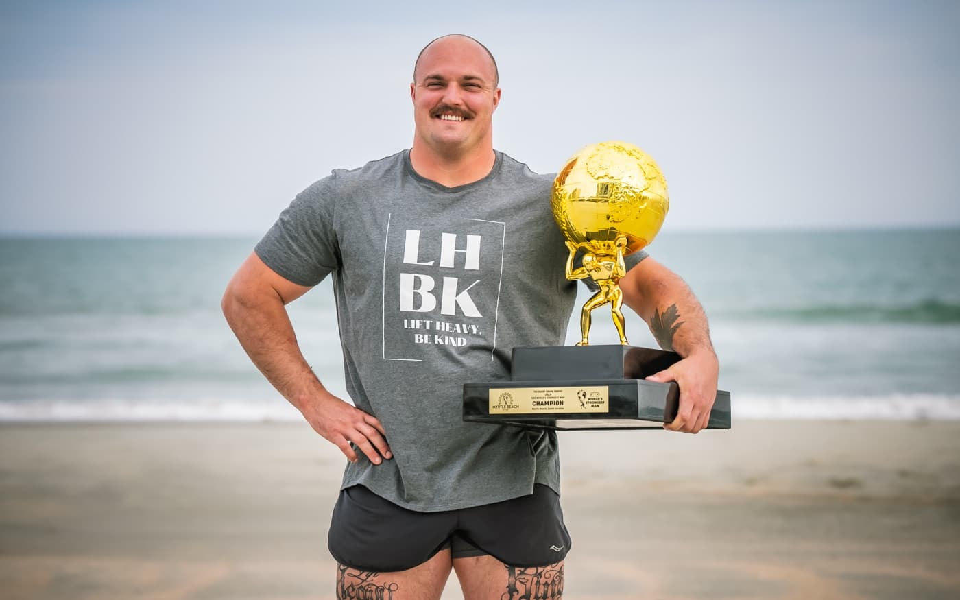 Mitchell Hooper on the beach with the 2023 World's Strongest Man trophy