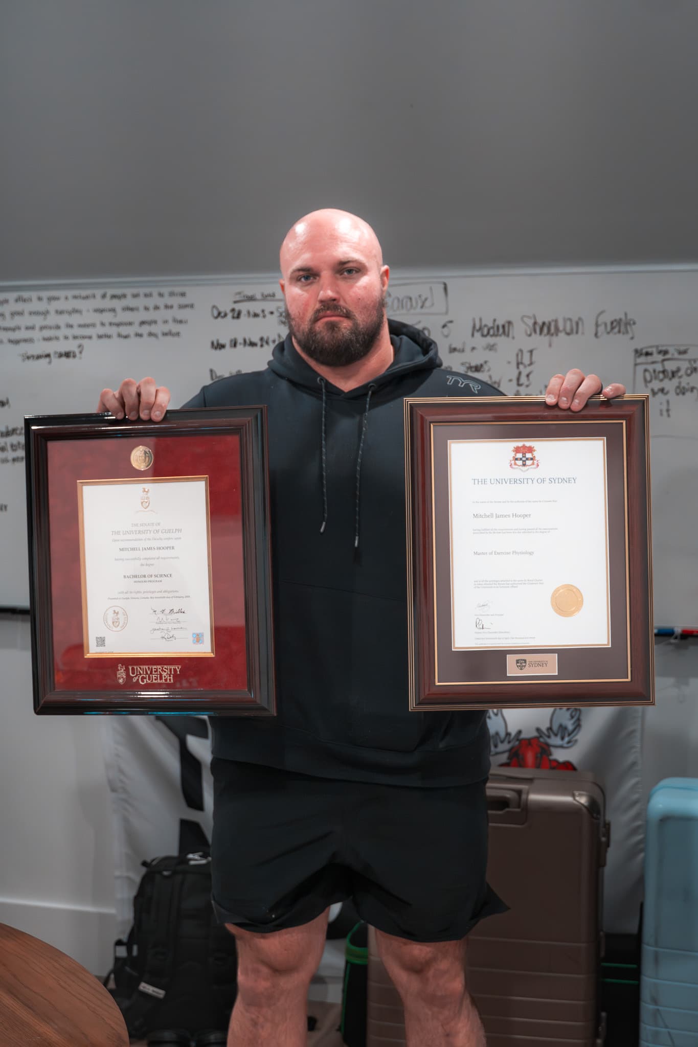 Mitchell Hooper holding his two framed university degrees