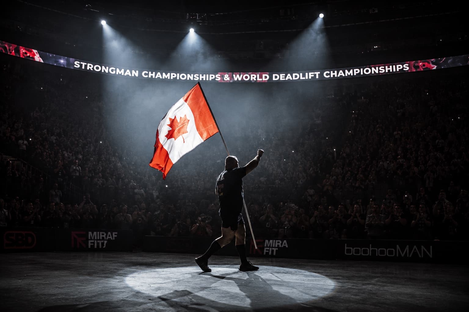Mitchell Hooper walking into a dark arena under a spotlight, carrying the Canadian flag